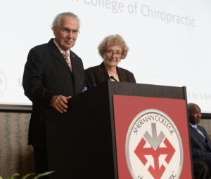 Sherman College founder and first president Dr. Thom Gelardi, with his wife, Dr. Betty Gelardi, addresses the group during the dedication ceremony for the Gelardi Student Center on the campus of Sherman College of Chiropractic. 